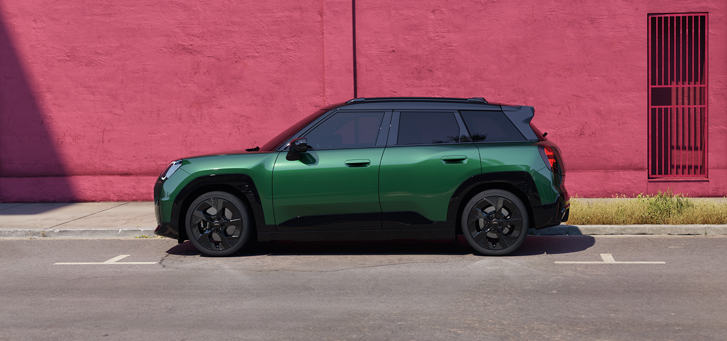 Stranski pogled na električni MINI Aceman v barvi British Racing Green s črno streho na ulici.