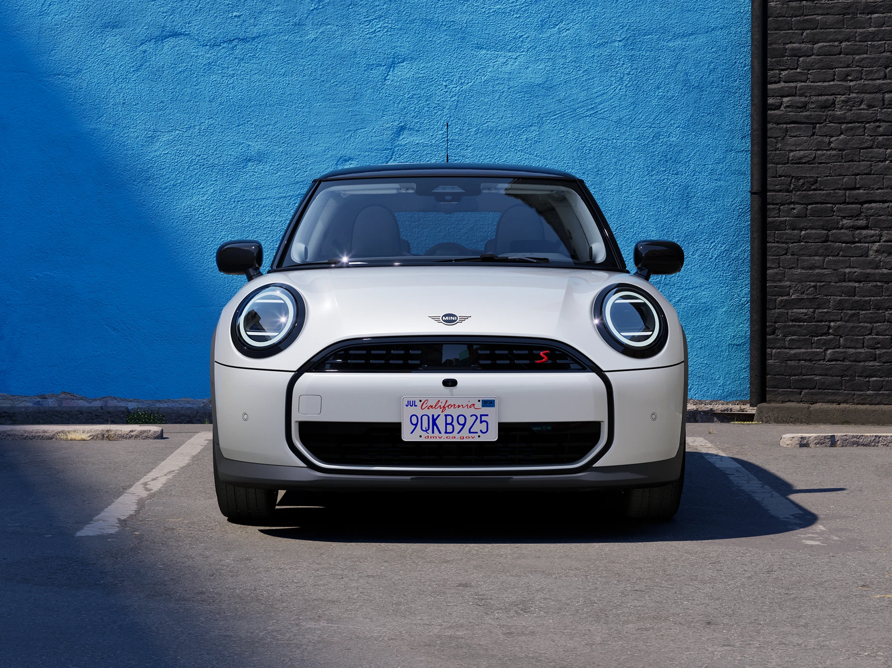 Pogled od spredaj na MINI Cooper v barvi Nanuq White s črno streho na parkirišču.