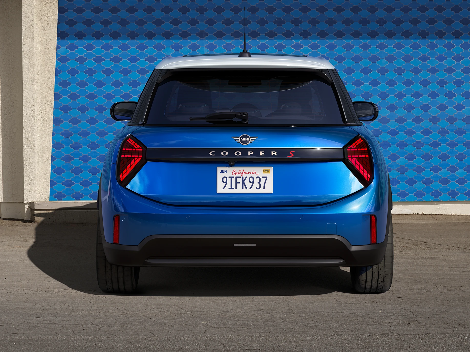 Pogled od zadaj na MINI Cooper s petimi vrati v barvi Icy Sunshine Blue z večbarvno streho v modrem odtenku.
