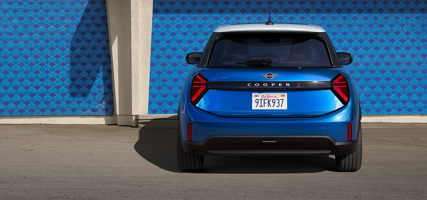Pogled od zadaj na MINI Cooper s petimi vrati v barvi Icy Sunshine Blue z večbarvno streho v modrem odtenku.
