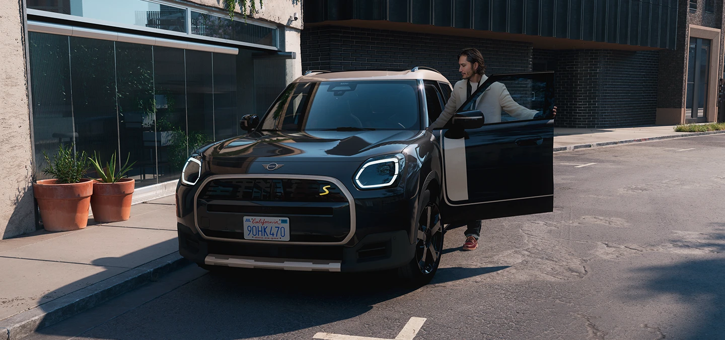 Pogled od spredaj na električni MINI Countryman v barvi Midnight Black z izrazito streho Vibrant Silver na ulici.