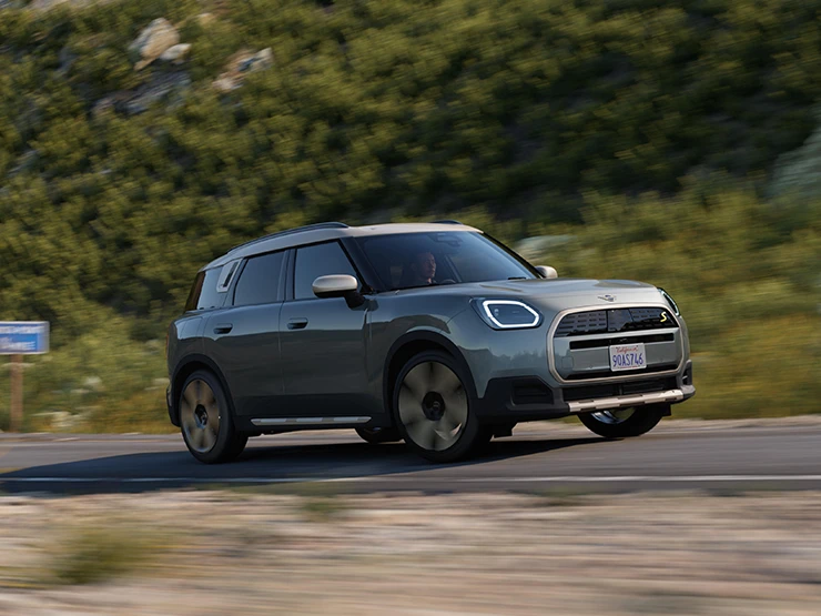 Stranski pogled na električni MINI Countryman v barvi Smokey Green s streho Vibrant Silver med vožnjo na terenu.
