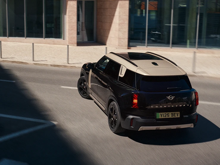 Zgornji pogled od zadaj na električni MINI Countryman v barvi Midnight Black s streho Vibrant Silver na parkirišču.