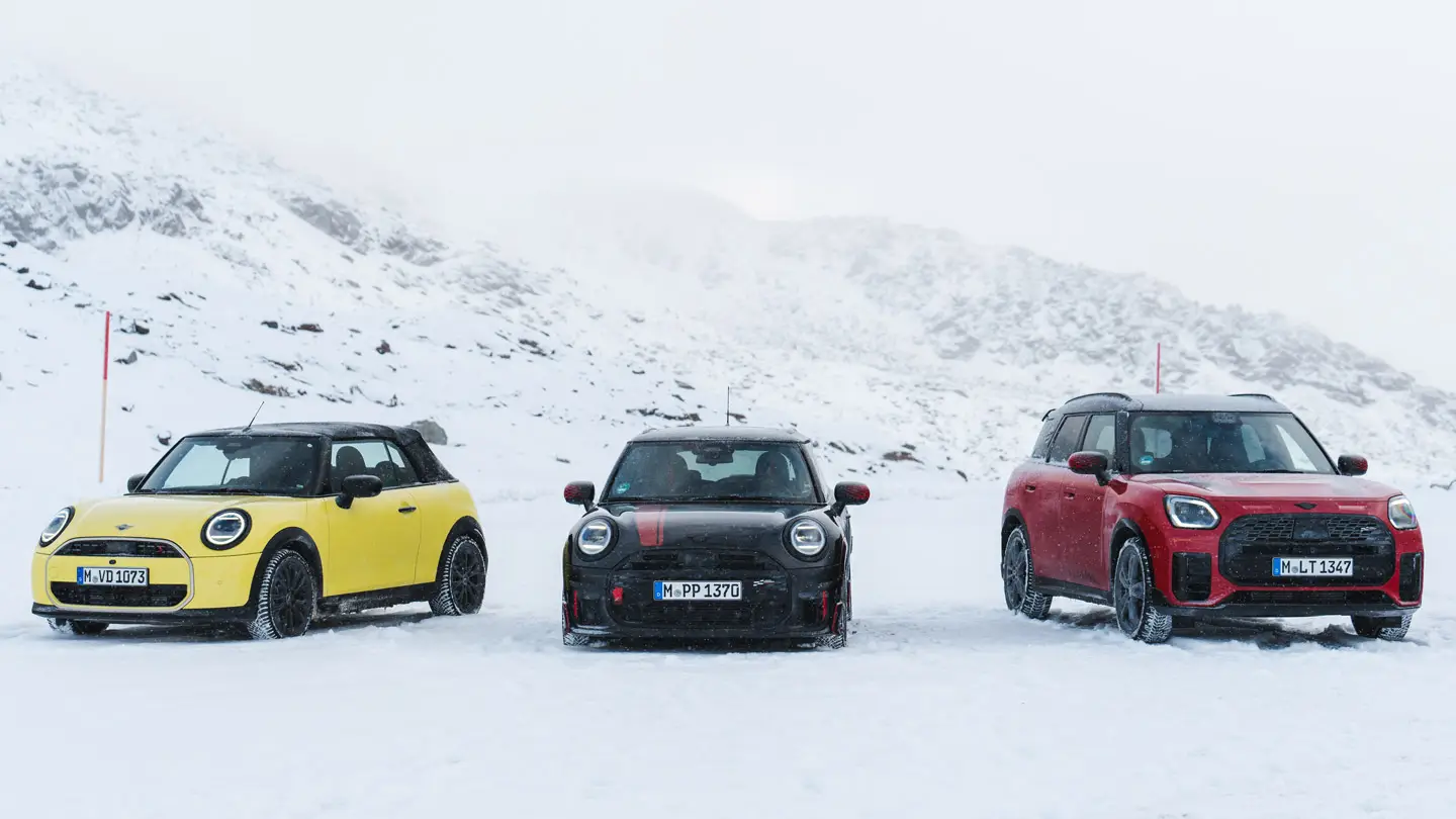 MINI Cooper Cabrio v barvi Sunny Side Yellow, MINI John Cooper Works v barvi Midnight Black II in MINI Countryman Cooper v barvi Chilli Red – parkiran na zasneženi gorski cesti, pogled od spredaj.