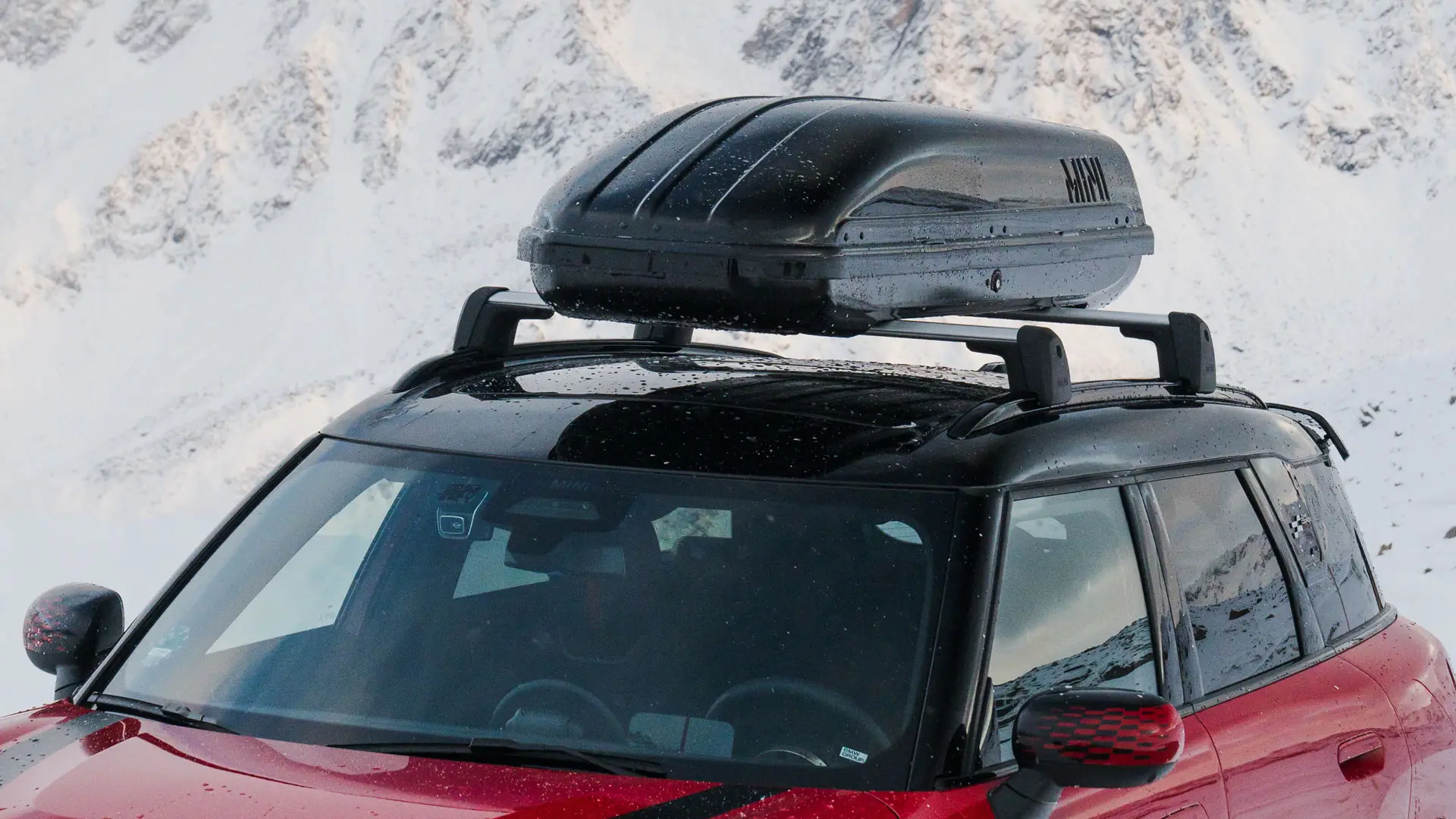 MINI Countryman v barvi Chili Red II s 320-litrskim strešnim kovčkom MINI v črni barvi.