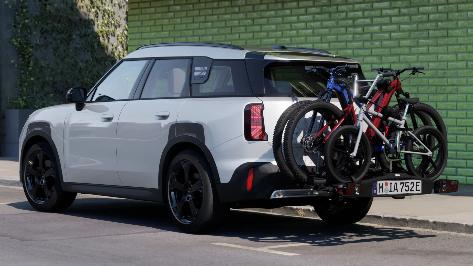 MINI Aceman v barvi Nanuq White z nameščenim zadnjim nosilcem za kolesa MINI Pro 3.0, na katerem stav dve gorski kolesi in otroško kolo.