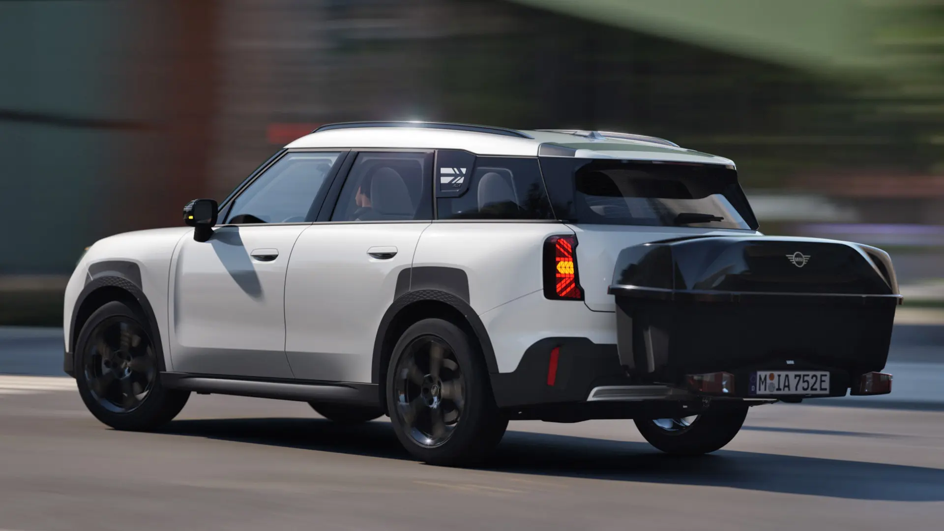 Pogled od zadaj s strani na MINI Aceman v barvi Nanuq White z nameščenim zadnjim nosilcem za kolesa MINI in zadnjim kovčkom MINI. 