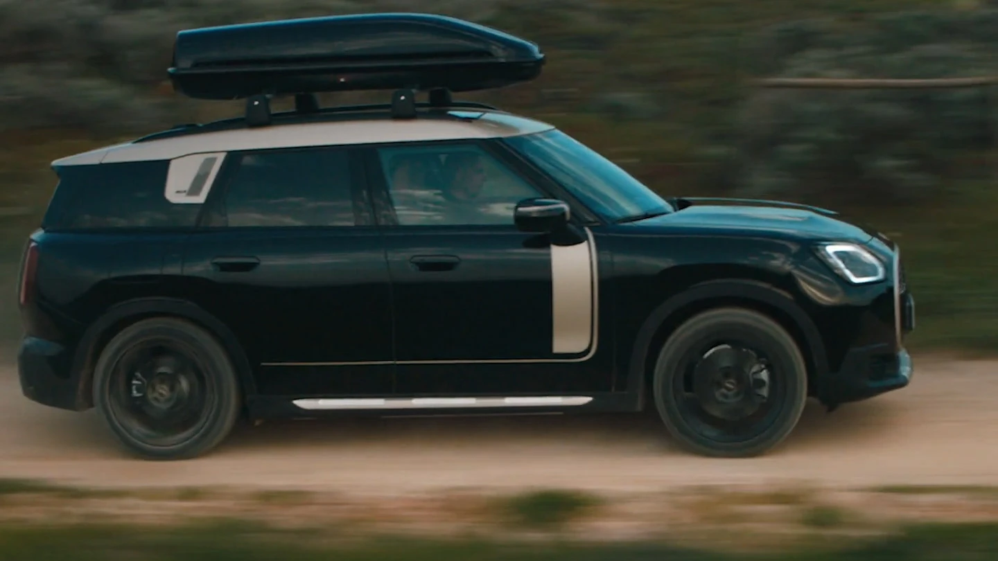 MINI Countryman v kovinski barvi Midnight Black z 19-palčnimi kolesi John Cooper Works Runway Spoke v črni barvi, ki vozi po terenu. 