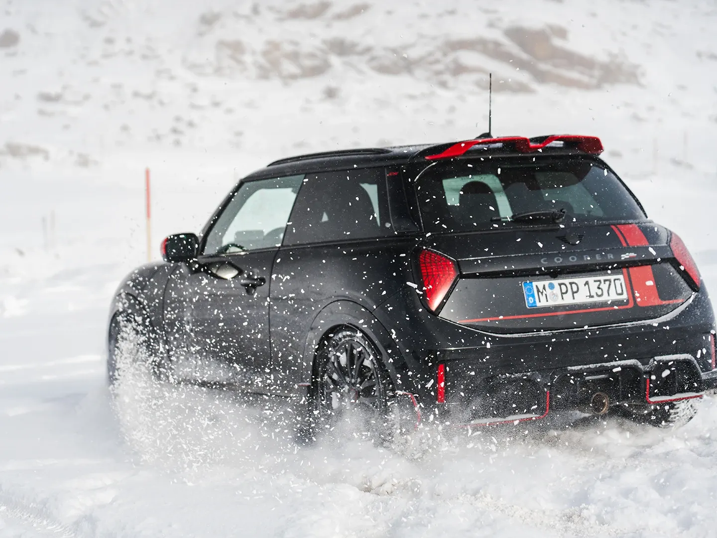 Pogled od zadaj na vozilo MINI Cooper JCW med vožnjo po snegu.