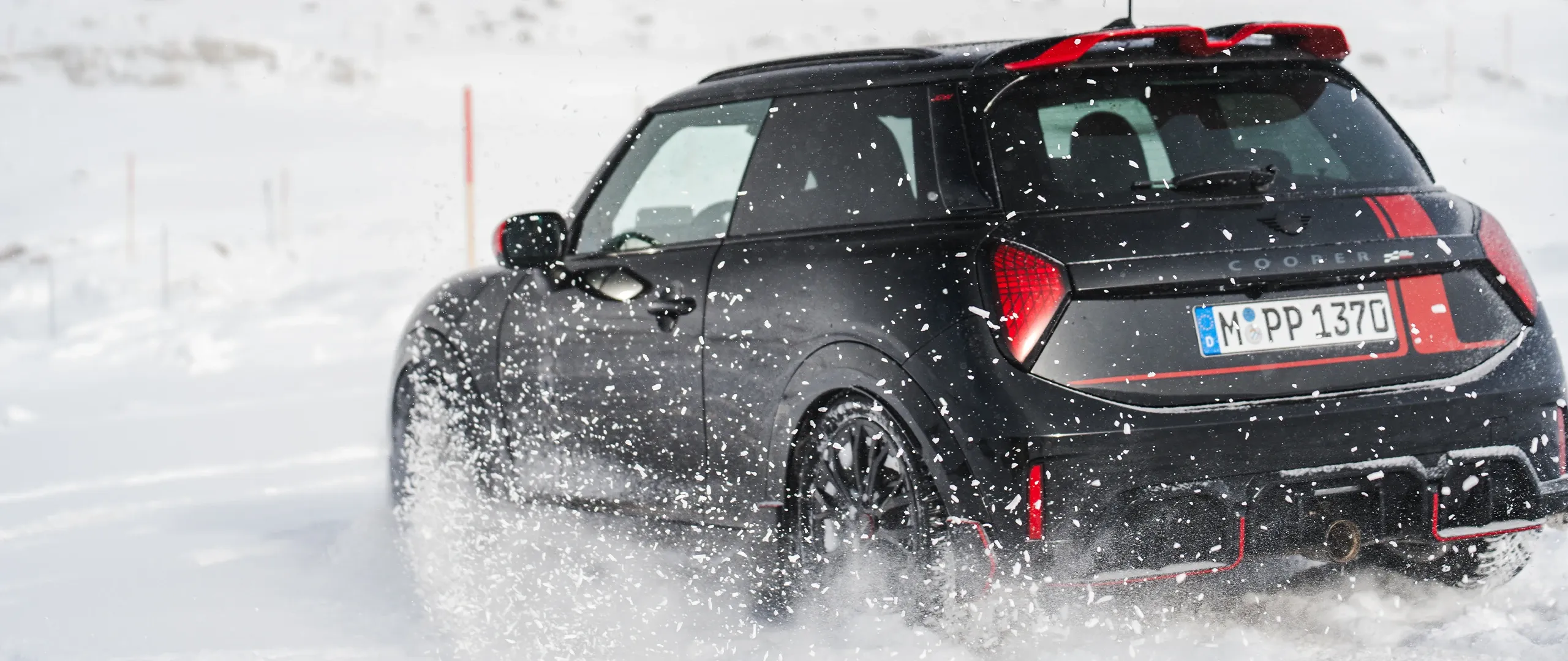 Pogled od zadaj na vozilo MINI Cooper JCW med vožnjo po snegu.
