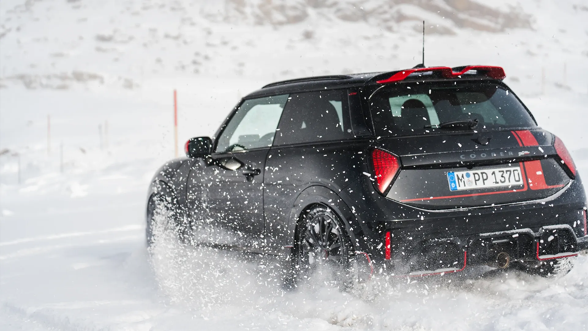 Pogled od zadaj na vozilo MINI Cooper JCW med vožnjo po snegu.
