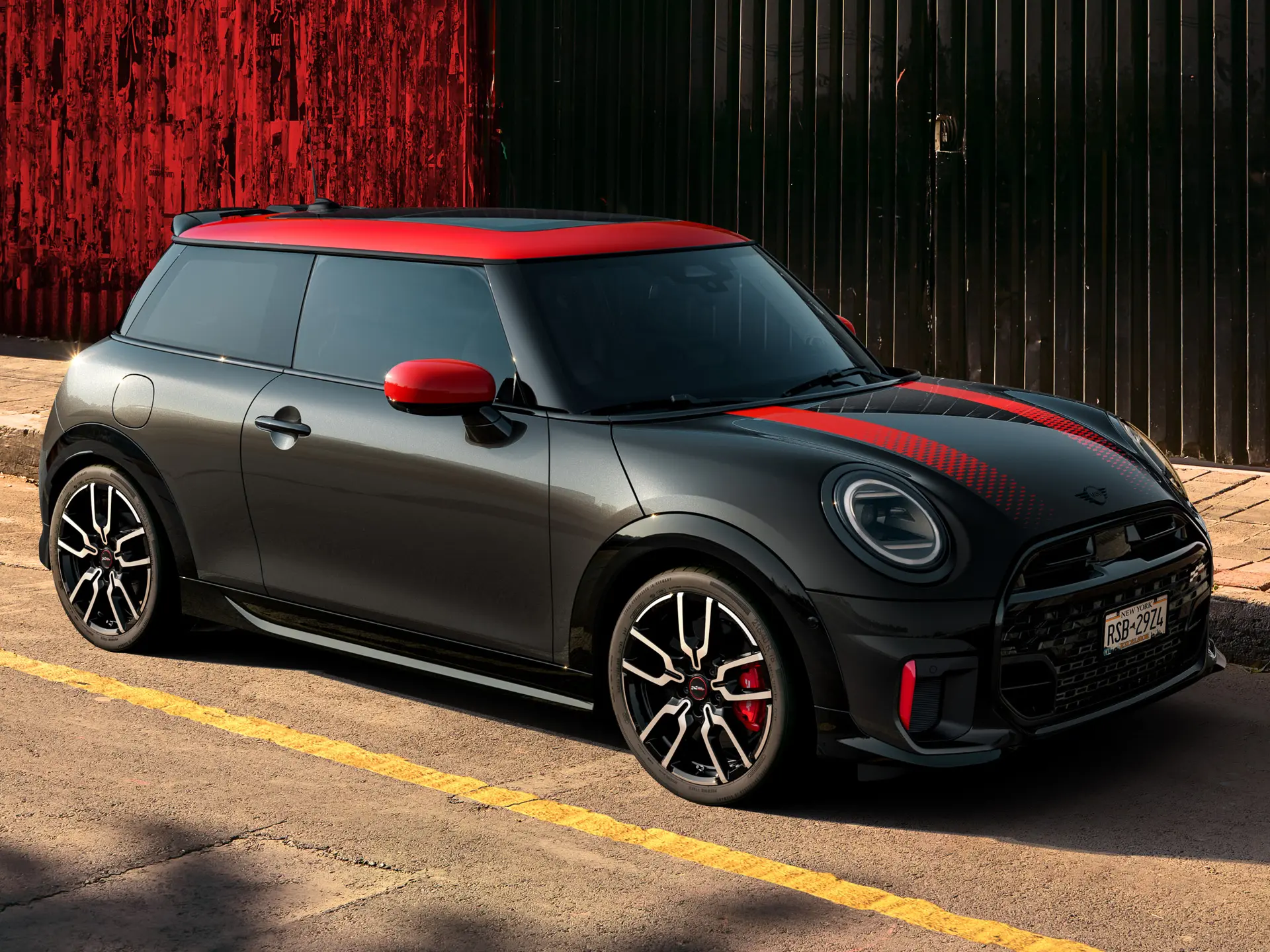 MINI John Cooper Works s tremi vrati v barvi Midnight Black, s streho in pokrovi zunanjih ogledal v barvi Chili Red ter rdečimi športnimi črtami, stranski pogled, parkiran na ulici