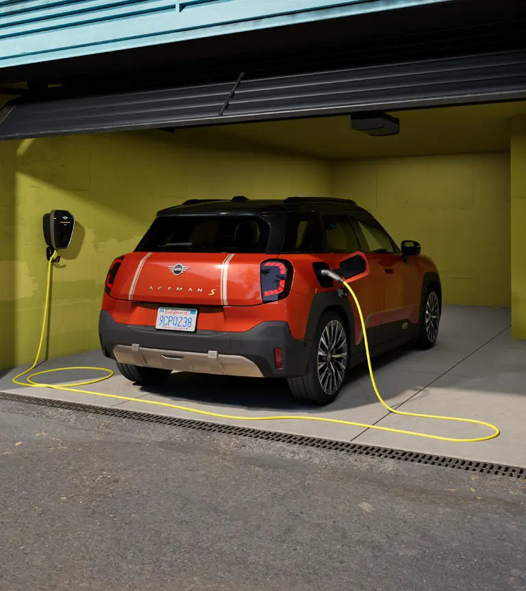 Popolnoma električni MINI Aceman S se polni z MINI Wallbox Plus, pogled od zadaj, parkiran v garaži.