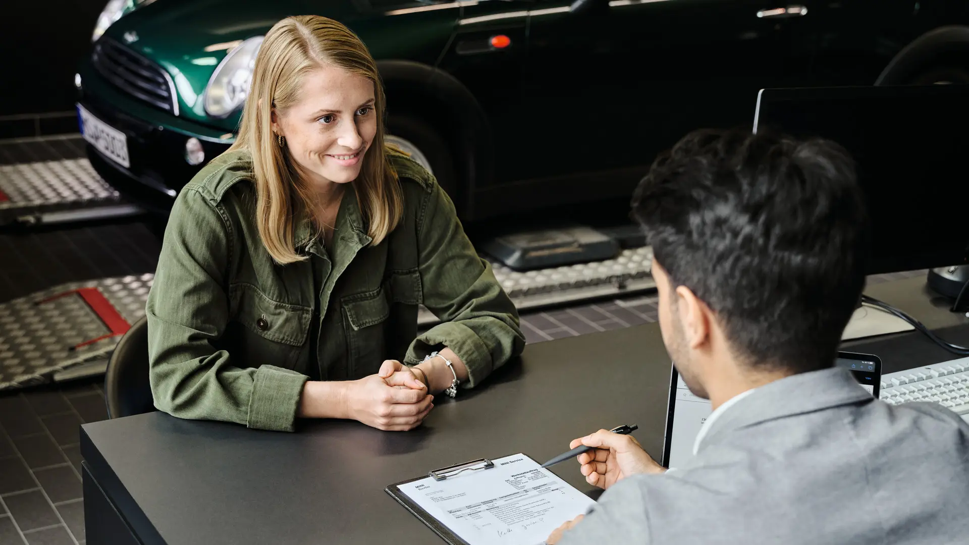 Pooblaščeni servis MINI s svetovalcem, ki stranki razlaga možnosti servisnih storitev, oba sedita za mizo