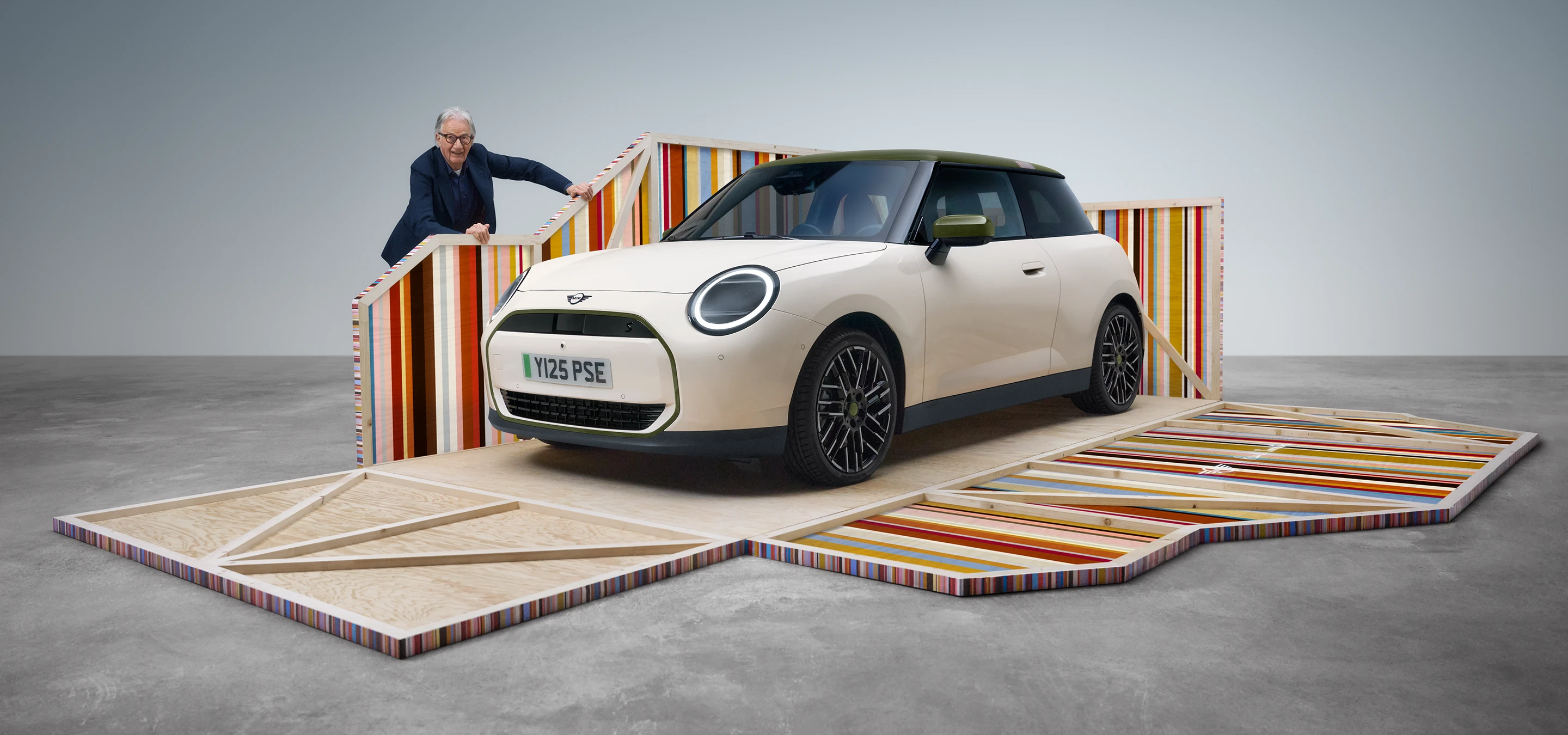 Pogled od spredaj na električni MINI Cooper Paul Smith Edition v barvi Inspired White z oblikovalcem Paulom Smithom