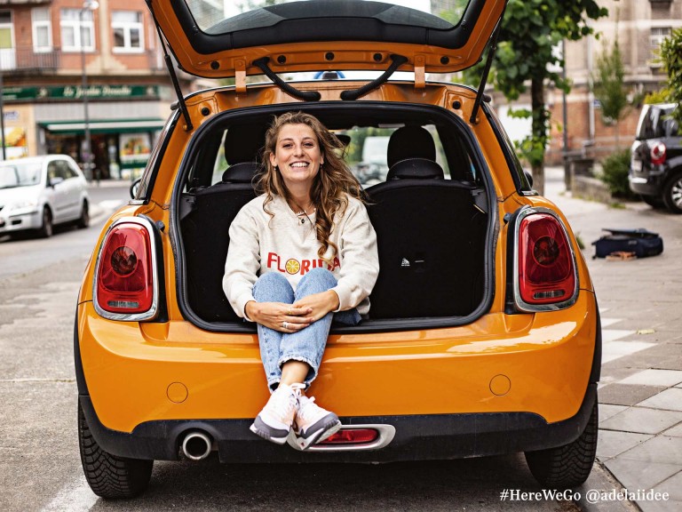 MINI s tremi vrati v barvi Volcanic Orange z žensko veselega razpoloženja, ki sedi v prtljažniku